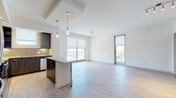 This contemporary single-floor residence offers a thoughtfully designed open-concept layout that seamlessly connects the kitchen, dining, and living areas. Light wood-tone flooring runs throughout, complementing the clean white walls and creating a bright, cohesive aesthetic.

The kitchen is a standout feature, equipped with rich dark wood cabinetry, granite countertops, a tile backsplash, and a full suite of stainless steel appliances, including a range, microwave, and dishwasher. A peninsula with pendant lighting provides additional counter space and serves as a casual dining or gathering point. Large windows and a glass door in the living area flood the open space with natural light and offer views of the surrounding neighborhood.

The bedrooms are generously sized with the same wood-tone flooring and roller shade windows that allow for flexible light control. The primary suite includes access to a spacious walk-in closet with built-in shelving and hanging rods, providing ample storage. Both bathrooms feature striking marble-style tile flooring and wall surrounds. The primary bathroom includes a glass-enclosed walk-in shower with a bench, a dual-sink vanity with dark cabinetry, and a large illuminated mirror. The secondary bathroom also features a glass-enclosed shower with marble tile detailing.