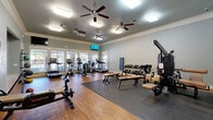 Located at 1900 Westview Blvd in Conroe, Texas, this well-equipped fitness center offers a thoughtfully designed single-floor exercise space. The room features warm hardwood flooring throughout, transitioning to protective rubber matting in the strength and weight training zones. Crown molding and soft blue-gray walls lend a polished, welcoming aesthetic to the space.

Natural light flows in through a generous bank of large windows along one wall, fitted with blinds for adjustable brightness. Multiple ceiling fans ensure consistent air circulation, complemented by overhead flush-mount lighting for well-lit workouts at any time of day. A wall-mounted flat-screen television adds entertainment options for cardio sessions.

The cardio area is outfitted with treadmills, elliptical trainers, and a recumbent bike, all positioned to face the windows and exterior views. The strength training section includes a multi-station cable machine, adjustable weight benches, and a full dumbbell rack with a wide range of free weights. A yoga mat station and medicine ball rack provide additional options for functional fitness and flexibility training. The open layout offers ample room to move between stations comfortably, making this fitness center a practical and well-rounded facility for residents of the Westview Blvd community.