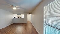 This single-story unit offers an efficient and cohesive layout, with warm wood-look flooring running continuously throughout all rooms, creating a unified and clean aesthetic. Neutral white walls and white trim complement the flooring, lending a bright, move-in-ready feel to the entire space.

The combined living and kitchen area forms the heart of the unit. The living room features a ceiling fan with light fixture and a window with blinds allowing natural light to filter in, alongside a front entry door equipped with a keypad lock. The kitchen is positioned behind a raised breakfast bar with granite-style countertops, offering a pass-through opening to the living area. White cabinetry, stainless steel appliances, a range hood, and a window above the sink complete the kitchen.

A hallway connects the main living area to the private spaces. The bedroom is a comfortable size, featuring two windows for natural light, a ceiling fan, and a double-door closet. The bathroom includes a granite-topped vanity with white cabinetry, a tub-shower combination, and wood-look flooring consistent with the rest of the unit.