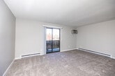 This single-floor unit offers a well-organized layout designed for practical, comfortable living. The living area is generously proportioned, featuring plush carpeting, a textured ceiling, and a wall-mounted air conditioning unit. A sliding glass door fills the space with natural light and opens directly onto a private balcony with outdoor views, while baseboard heating runs along the perimeter walls for year-round comfort.

The kitchen is cleanly appointed with white shaker-style cabinetry, light stone-finish countertops, and wood-look vinyl flooring. Black appliances—including a range, dishwasher, and refrigerator—provide a crisp contrast to the bright cabinetry. A pass-through counter connects the kitchen to the adjacent living area, enhancing the open feel of the space.

The bedrooms are carpeted and neutral in tone, each offering windows that bring in natural light. Ceiling fans are present in select rooms, and closet access is conveniently located. The bathroom features a full tub-shower combo, a white vanity with ample storage, and wood-look tile flooring, completing the unit with a clean, functional finish.