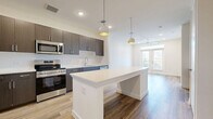 Located at 3842 W Northwest Hwy in Dallas, TX, this well-appointed 1-bedroom, 2-bathroom unit offers a thoughtfully designed open-concept layout. The combined kitchen and living area serves as the heart of the home, showcasing wood-look flooring, recessed lighting, and a ceiling fan. The kitchen is outfitted with dark espresso cabinetry, stainless steel appliances including a refrigerator, range, and microwave, and a sleek white quartz island with built-in pendant lighting and a wine cooler beneath. French doors lead from the living area to a private balcony, filling the space with natural light. The bedroom features plush carpeting, a large window with outdoor views, and a ceiling fan. The primary bathroom is elegantly finished with dark wood vanity cabinetry, white quartz countertops, wood-look flooring, and a glass-enclosed walk-in shower adorned with marble-style tile. A walk-in closet is conveniently accessible from the bathroom. Additional highlights include two closets, a dedicated laundry area, and a utility room, ensuring ample storage and everyday functionality throughout this modern Dallas residence.