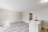 Located at 3203 Orange St in Greensboro, NC, this single-floor, one-bedroom, one-bathroom unit offers a practical and well-organized layout with clean, neutral finishes throughout. The living area features light-toned luxury vinyl plank flooring that reflects natural light from a large front-facing window, creating a bright and welcoming atmosphere. Baseboard heating runs along the walls, and a textured ceiling adds a classic residential character to the space. The kitchen is defined by a peninsula counter with a marble-style surface and an integrated sink with a modern gold-toned faucet, providing both functionality and a visual focal point that separates the kitchen from the living area. The bedroom is generously proportioned, finished with soft carpeting underfoot and a window that allows for natural light and ventilation, complemented by a wall-mounted AC unit. A dedicated closet off the bedroom features dual wire shelving racks, offering organized storage space with light LVP flooring. The full bathroom includes a tub-shower combination, toilet, and wood-look tile flooring, finished in a clean, all-white palette. The overall design is cohesive, with warm beige tones, white trim, and consistent finishes that give the unit a tidy, move-in-ready appeal.