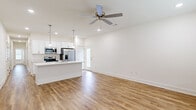 Located at 9549 Glen Rd in Bentonville, Arkansas, this single-story, 5-bedroom, 2-bathroom home offers a clean, modern aesthetic with consistent wood-look flooring and crisp white walls throughout. The open-concept kitchen and living area serves as the heart of the home, featuring a large center island with a white quartz countertop and undermount sink, white shaker-style cabinetry, stainless steel appliances including a French door refrigerator, electric range, and built-in microwave, all illuminated by stylish pendant lighting and recessed fixtures. The living area flows naturally from the kitchen and is finished with a ceiling fan. Each of the five bedrooms continues the bright, neutral palette with warm wood-look flooring and ceiling fans. The spacious primary bedroom includes a walk-in closet. The two bathrooms are well-appointed with white shaker vanities, quartz countertops, and wood-look flooring; one features a tub/shower combination while the other offers a glass-enclosed walk-in shower. A dedicated laundry room with washer and dryer hookups adds everyday convenience. The home's clean lines, neutral finishes, and functional layout make it a well-organized and comfortable living space.