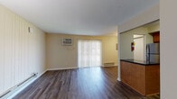 This one-bedroom unit offers a thoughtfully designed single-level layout that balances comfort and functionality. The open living area is finished with rich, dark hardwood-style flooring that extends throughout, complemented by warm, neutral-toned walls that create a bright and welcoming atmosphere. A sliding glass door fitted with vertical blinds fills the living space with natural light and provides access to the outdoors, while a wall-mounted air conditioning unit and baseboard heating ensure year-round comfort.

The kitchen is positioned adjacent to the living area and features warm wood cabinetry, dark granite-style countertops, a double stainless steel sink, and stainless steel appliances including a refrigerator, microwave, and range. A peninsula counter separates the kitchen from the living space, adding both visual definition and functionality.

The bedroom is a serene retreat finished with plush carpeting and a large double window dressed with horizontal blinds, offering pleasant outdoor views and ample natural light. Baseboard heating keeps the room comfortable throughout the seasons.

The bathroom is clean and practical, offering a full tub-and-shower combination, a vanity with warm wood cabinetry, and overhead storage cabinets in a crisp white finish. The overall layout is efficient and cohesive, making this a comfortable and move-in-ready living space.