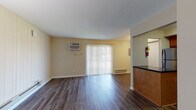 This one-bedroom unit offers a thoughtfully designed single-level layout that balances comfort and functionality. The open living area is finished with rich, dark hardwood-style flooring that extends throughout, complemented by warm, neutral-toned walls that create a bright and welcoming atmosphere. A sliding glass door fitted with vertical blinds fills the living space with natural light and provides access to the outdoors, while a wall-mounted air conditioning unit and baseboard heating ensure year-round comfort.

The kitchen is positioned adjacent to the living area and features warm wood cabinetry, dark granite-style countertops, a double stainless steel sink, and stainless steel appliances including a refrigerator, microwave, and range. A peninsula counter separates the kitchen from the living space, adding both visual definition and functionality.

The bedroom is a serene retreat finished with plush carpeting and a large double window dressed with horizontal blinds, offering pleasant outdoor views and ample natural light. Baseboard heating keeps the room comfortable throughout the seasons.

The bathroom is clean and practical, offering a full tub-and-shower combination, a vanity with warm wood cabinetry, and overhead storage cabinets in a crisp white finish. The overall layout is efficient and cohesive, making this a comfortable and move-in-ready living space.