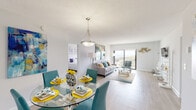 Located on the 12th floor at 100 Kings Point Dr in Sunny Isles Beach, Florida, this residence offers a thoughtfully designed single-floor layout with an open-concept living and dining area that flows seamlessly toward a glass sliding door, framing stunning panoramic views of the Atlantic Ocean. Light wood-style flooring runs throughout the main living spaces, complementing the bright white walls and textured ceilings that lend the interior a clean, contemporary feel. The dining area features a pendant light fixture and opens directly into the living room, creating an inviting, connected atmosphere. The kitchen is well-equipped with white cabinetry, granite countertops, black appliances, and ample storage — ideal for everyday functionality. The primary bedroom is generously sized with carpeted flooring, a walk-in closet, and an en-suite bathroom featuring granite countertops and white cabinetry. A second bedroom benefits from large windows with sweeping ocean and city views. A second full bathroom mirrors the refined finishes found throughout, with granite surfaces and white cabinetry. The overall ambiance is bright, airy, and coastal — perfectly suited to the Sunny Isles Beach lifestyle.