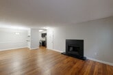 This single-story residence offers a thoughtfully arranged layout with a blend of warm hardwood flooring and practical finishes throughout. The spacious living area serves as the heart of the home, anchored by a striking black-tiled fireplace that adds a bold focal point to the room. Natural light filters in through multiple windows fitted with blinds, while a door provides direct access to a private deck overlooking a lush, tree-lined outdoor setting.

The open layout connects the living space to the kitchen, which is equipped with dark cabinetry, granite-style countertops, stainless steel appliances including a refrigerator, electric range, and microwave. Notably, in-unit laundry is seamlessly integrated into the kitchen area, with a washer and dryer positioned alongside the cabinetry for added convenience.

The bedroom features plush carpeting and a window that brings in natural light with views of the surrounding greenery. A hallway connects the bedroom to the rest of the unit, where a full bathroom includes a tiled tub-shower combination with chrome fixtures. Textured ceilings and neutral gray walls are consistent throughout, lending the space a clean, cohesive aesthetic.
