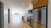 Located on Wilshire Boulevard in the heart of Los Angeles, this modern single-floor unit showcases a clean, contemporary design throughout. Light wood flooring runs continuously across the open-plan living areas, creating a warm and cohesive aesthetic that complements the crisp white walls and recessed lighting overhead.

The kitchen is a standout feature, outfitted with a full suite of stainless steel appliances including a French door refrigerator, electric range, built-in microwave, and dishwasher. Two-tone cabinetry pairs white upper cabinets with warm wood lower cabinets, accented by a marble-style tile backsplash and a sleek white countertop. In-unit washer and dryer hookups are conveniently integrated alongside the kitchen cabinetry.

The bedroom is generously proportioned, bathed in abundant natural light through a wide, floor-to-ceiling window offering open city views. A sliding glass-panel closet provides built-in storage with a modern touch.

The bathroom features a combination tub and shower with vertically stacked tile surround, a geometric-patterned tile floor, a wall-mounted vanity with wood cabinetry, and a white stone countertop with an undermount sink. The overall design of the unit reflects a refined urban aesthetic, well-suited to the dynamic Koreatown/Wilshire corridor location.