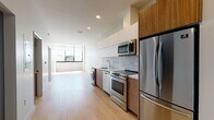 Located on Wilshire Boulevard in the heart of Los Angeles, this modern single-floor unit showcases a clean, contemporary design throughout. Light wood flooring runs continuously across the open-plan living areas, creating a warm and cohesive aesthetic that complements the crisp white walls and recessed lighting overhead.

The kitchen is a standout feature, outfitted with a full suite of stainless steel appliances including a French door refrigerator, electric range, built-in microwave, and dishwasher. Two-tone cabinetry pairs white upper cabinets with warm wood lower cabinets, accented by a marble-style tile backsplash and a sleek white countertop. In-unit washer and dryer hookups are conveniently integrated alongside the kitchen cabinetry.

The bedroom is generously proportioned, bathed in abundant natural light through a wide, floor-to-ceiling window offering open city views. A sliding glass-panel closet provides built-in storage with a modern touch.

The bathroom features a combination tub and shower with vertically stacked tile surround, a geometric-patterned tile floor, a wall-mounted vanity with wood cabinetry, and a white stone countertop with an undermount sink. The overall design of the unit reflects a refined urban aesthetic, well-suited to the dynamic Koreatown/Wilshire corridor location.
