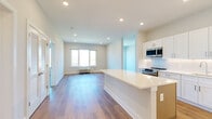 This single-floor residence is designed with a clean, contemporary aesthetic and an efficient, open layout. The heart of the space is the expansive kitchen, which serves as a focal point with its crisp white shaker cabinetry extending to the ceiling, a large quartz island with generous countertop space, and a full suite of stainless steel appliances including a range, microwave, dishwasher, and refrigerator. A subway tile backsplash adds textural detail, while recessed lighting illuminates the space. Light wood-tone flooring flows throughout the kitchen and into the open living area, reinforcing a sense of continuity and spaciousness. The living area receives natural light through a window with outdoor views of the surrounding neighborhood and green space beyond.

The bedrooms are finished with plush neutral carpeting and feature dedicated closet space with built-in shelving. Each room maintains the unit's neutral color palette, creating a calm and versatile environment. The bathroom features light tile flooring, a dark-cabinetry vanity with a white countertop, and clean white walls accented by brushed nickel hardware. Overall, the space presents a well-appointed, move-in-ready interior with modern finishes throughout.