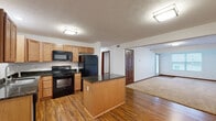 This efficiently designed single-floor residence offers a thoughtful layout across one bedroom, one bathroom, and a dedicated closet. The open-concept kitchen flows seamlessly into the living area, creating a connected and functional living space. The kitchen is outfitted with warm honey-toned cabinetry, dark granite countertops, a central island with matching granite, and a full suite of black appliances including a range, microwave, refrigerator, and dishwasher. Hardwood-style flooring grounds the kitchen and living area, adding warmth and visual continuity throughout. The living room is bright and open, featuring neutral carpet, a window with exterior views, and a glass-panel door that introduces additional natural light. The bedroom offers plush carpeting, a ceiling fan with light fixture, a window for natural light, and rich wood-trimmed double doors leading to a dedicated closet complete with built-in shelving. The bathroom is clean and functional, featuring a full soaking tub with shower, grab bars, and tile flooring. Textured ceilings and warm wood baseboards throughout lend a cohesive, classic character to the entire residence.