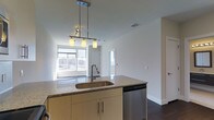 Located at 900 Luxor Lane in Norristown, Pennsylvania, this single-floor residence offers a thoughtfully designed open-concept layout with clean, modern finishes throughout. The kitchen serves as a central focal point, anchored by a large island with granite countertops, an undermount stainless steel sink, and light wood cabinetry that provides ample storage. A stainless steel dishwasher adds to the kitchen's functional appeal, while a stylish three-pendant light fixture with cylindrical shades hangs overhead, providing warm, focused illumination over the island workspace. The open flow between the kitchen and the living area creates a spacious, connected feel ideal for both everyday living and entertaining. Dark hardwood flooring runs throughout, providing a rich contrast to the bright white walls and ceilings. Large windows along the far wall flood the living space with natural light, offering views of the surrounding landscape. The overall ambiance is clean, contemporary, and welcoming, with a neutral palette that allows for versatile interior styling. This well-appointed single-level home combines practical design with modern aesthetic sensibilities in a convenient Norristown location.
