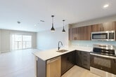 Located at 19 Hemans St in Worcester, MA, this well-designed one-bedroom, one-bathroom unit offers a thoughtful layout across a single floor. The open-concept living, dining, and kitchen area forms the heart of the space, finished with light wood-look flooring that flows throughout. The modern kitchen is a standout feature, showcasing two-tone cabinetry with warm walnut uppers and dark lower cabinets, crisp white quartz countertops, a light blue glass tile backsplash, and a full suite of stainless steel appliances including a range, microwave, dishwasher, and refrigerator. Stylish black pendant lights hang above the peninsula, adding a contemporary touch. The open living area is bathed in natural light and connects directly to a private balcony through sliding glass doors, offering views of the surrounding Worcester cityscape and treeline. The bedroom is carpeted for comfort, features a double-door closet, and includes a window with the same pleasant outdoor views. The bathroom is finished with large-format gray floor tiles, a tiled tub/shower surround, and matte black fixtures. Additional spaces include a hallway, entrance, two closets, a laundry area, and a utility room, rounding out the unit's practical offerings.
