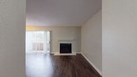 This single-story unit presents a practical and comfortable layout across several well-defined living spaces. The living room serves as the central gathering area, highlighted by a wood-burning fireplace with a white mantel and a sliding glass door fitted with vertical blinds that allow natural light to filter in while providing access to an outdoor area. Rich, dark hardwood-style flooring runs throughout the main living areas, adding warmth and visual continuity.

Adjacent to the living room, the galley-style kitchen is efficiently designed with cabinetry finished in a soft gray tone, granite-style countertops lining both sides, and white appliances including a refrigerator, range, and dishwasher. The dark flooring continues into the kitchen, maintaining a cohesive aesthetic.

The bedrooms are comfortably sized, featuring neutral wall tones, plush wall-to-wall carpeting, and windows that bring in natural light. The spaces offer a calm, understated atmosphere well-suited for rest.

The bathroom includes a full tub-shower combination, a toilet, and a vanity topped with a granite-style surface and paired with a large mirror. The overall design of the unit emphasizes functionality, with a neutral color palette and consistent finishes throughout.