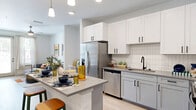 Located at 1148 N Main St in Jacksonville, FL, this thoughtfully designed one-bedroom, one-bathroom residence offers a cohesive modern aesthetic throughout its efficiently utilized single floor. The open-concept kitchen and living area serves as the heart of the home, featuring light wood-look flooring, recessed lighting, and pendant lights over a central island with bar seating. The kitchen is outfitted with two-tone cabinetry — white uppers and gray lowers — complemented by a white subway tile backsplash, stainless steel appliances including a French door refrigerator and dishwasher, and a matte black faucet. The living area receives natural light through a glass door that opens to a private balcony. The bedroom offers plush carpeting, a ceiling fan, and windows with outdoor views, creating a comfortable and restful retreat. The full bathroom features light wood-look flooring, a gray shaker-style vanity with a quartz countertop, a large mirror, and a glass-enclosed walk-in shower with white subway tile and matte black fixtures. A stacked in-unit washer and dryer provide added convenience. The overall palette of whites, grays, and natural wood tones creates a clean, contemporary ambiance throughout.