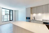 Located at 1320 4th St NE in Washington, DC, this thoughtfully designed one-bedroom, one-bathroom residence offers a clean, modern aesthetic throughout its well-appointed single floor. The entrance leads down a bright, wood-floored hallway lined with louvered closet doors, providing generous storage from the moment you arrive. The open-concept living, dining, and kitchen area serves as the heart of the home, bathed in natural light from expansive floor-to-ceiling windows with sleek black frames that frame urban cityscape views. The kitchen is a standout feature, equipped with light wood cabinetry extending to the ceiling, a large waterfall-edge island, quartz countertops, stainless steel appliances including a gas range, built-in microwave, and refrigerator, all complemented by under-cabinet lighting. Wide-plank hardwood flooring flows seamlessly throughout the main living areas. The bedroom offers a serene retreat with its own generous window overlooking the city. A separate den provides flexible additional space. The bathroom features distinctive hexagonal tile flooring, a light wood floating vanity with a white countertop, mirrored medicine cabinet, and matte black fixtures. Additional conveniences include dedicated laundry and utility rooms.