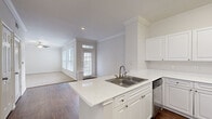 Located at 4807 Pin Oak Park in Houston, TX, this single-story, two-bedroom, two-bathroom home offers a thoughtfully designed layout with a clean, neutral aesthetic throughout. The open-concept kitchen and living area serves as the heart of the home, where a peninsula with a marble-look quartz countertop and a stainless steel sink anchors the space. White cabinetry with brushed nickel hardware, a stainless steel range, and a dishwasher complete the kitchen. Crown molding adds a refined touch throughout the common areas, while dark hardwood-style flooring in the kitchen flows into plush carpet in the living and bedroom spaces. The living room benefits from natural light through a windowed front door and blinds-covered windows. The generously sized primary bedroom features dual windows with blinds, a ceiling fan, crown molding, and access to a walk-in closet with wire shelving. A second carpeted bedroom also includes a window and ample closet space. Both bathrooms are finished in white with wide vanities, large mirrors, cabinet storage, and tub-shower combinations. The primary bath offers a wrap-around vanity layout. Three closets total and a dedicated laundry area round out the practical amenities of this well-appointed home.