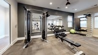 Located at 712 Promenade Place in Virginia Beach, Virginia, this fitness center offers a well-appointed, single-floor layout designed to support a comprehensive workout experience. The space is finished with durable, neutral-toned carpet tile flooring throughout, providing both comfort and functionality underfoot.

The cardio zone is generously equipped with multiple treadmills, Precor elliptical trainers, and a stationary bike, each positioned near a row of windows dressed with Roman shades that allow ample natural light to fill the room. Recessed lighting and ceiling-mounted fans with pendant-style fixtures ensure the space remains comfortable and well-illuminated at all times.

The strength training area features a cable crossover machine, a tiered dumbbell rack stocked with a wide range of free weights, flat weight benches, and a stability ball. A large wall-mounted mirror in this zone visually expands the space and allows users to monitor their form during exercise.

The walls are painted in a two-tone scheme — soft warm beige in the cardio area transitioning to a deeper charcoal gray accent in the weight training section — lending the space a modern, motivating atmosphere. Glass-paneled French doors provide access to an adjacent room, adding an open and connected feel to the overall layout. The fitness center is clean, thoughtfully organized, and well-suited for a full range of exercise routines.