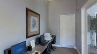 This single-floor office space offers a clean, professional environment designed for productivity and functionality. The room is characterized by impressively tall ceilings that lend a sense of openness and grandeur, complemented by neutral gray walls that create a calm, focused atmosphere throughout.

The primary workstation features a granite-topped desk that spans a generous length, providing ample surface area for computers, a printer, and office essentials. Two computer monitors are set up along the desk, alongside a keyboard and mouse, making the space well-equipped for multi-tasking or collaborative work. A mesh office chair offers ergonomic comfort at the workstation.

A classic six-panel white door with traditional molding adds a refined architectural touch to the room, consistent with the space's polished aesthetic. The flooring is covered in neutral-toned carpet, contributing to a quiet and comfortable working environment.

A large, elegantly framed botanical print adorns one wall, adding a decorative focal point that softens the professional setting. The overall ambiance balances functionality with understated sophistication, making this office space both practical and visually appealing for day-to-day professional use.