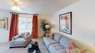 This single-story residence at 1710 N Woodmere Dr in Charleston, SC presents a well-organized layout designed for comfortable everyday living. The living room serves as the heart of the home, featuring plush carpeted flooring, a textured ceiling, and a large sliding window dressed with bold curtain panels that invite generous natural light and views of the surrounding greenery. The space comfortably accommodates multiple seating arrangements, making it ideal for relaxing or entertaining.

Adjacent to the living area, the dining room offers tile flooring and an elegant chandelier overhead, providing a welcoming setting for meals. A decorative mirror enhances the sense of space within the room.

The kitchen is efficiently laid out with ample white cabinetry for storage, a full suite of white appliances including a range, dishwasher, and refrigerator, complemented by tile flooring and under-cabinet lighting.

The bedrooms are carpeted and feature ceiling fans with light fixtures, windows with soft drapery, and a calm, restful ambiance. Each room offers a quiet retreat with views of the outdoors.

The bathroom includes a tiled tub-shower combination, tile flooring, and a vanity with mirror, maintaining a clean and functional aesthetic throughout. Overall, the residence offers a cohesive, neutral palette suited to Charleston living.
