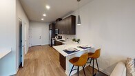 Located at 22551 Cabin Branch Ave in Boyds, Maryland, this thoughtfully designed studio unit offers a contemporary open-concept layout spread across a single floor. The space is unified by warm wood-tone flooring throughout, clean white walls, and recessed lighting that creates a bright, welcoming atmosphere.

The kitchen is a standout feature, showcasing rich dark-wood cabinetry extending to the ceiling, sleek white quartz countertops, a deep stainless steel undermount sink, a tasteful tile backsplash, and stainless steel appliances including a refrigerator, microwave, and dishwasher. A peninsula with pendant lighting above provides seating for two, serving as both a dining and casual workspace area.

A half-wall partition thoughtfully separates the sleeping area from the living and kitchen spaces, offering a sense of privacy while maintaining the open feel of the unit. The sleeping area accommodates a full-sized bed with ample room for additional furniture, such as a dresser. Natural light filters in through a window overlooking a wooded view, accompanied by a ceiling fan for added comfort.

The bathroom is well-appointed with a dark-wood vanity, a backlit mirror, white quartz countertop, and a tub-shower combination with a decorative curtain, all finished with wood-look tile flooring. The overall design is modern, cohesive, and functional.