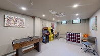 Located at 525 Main St in Hartford, Connecticut, this dedicated game room offers a lively and engaging recreational retreat within a compact, efficiently utilized footprint. The space is designed for entertainment and casual socializing, featuring a smooth light-toned floor, neutral-painted walls, and a clean, modern aesthetic throughout.

Recessed lighting illuminates the room evenly, complemented by a ceiling-mounted HVAC unit that ensures year-round comfort. A row of small windows along one wall allows natural light to filter in, offering glimpses of greenery outside. Colorful original artwork adorns the walls, adding a creative and vibrant character to the space.

The room is equipped with a combination foosball and ping-pong table as its centerpiece, flanked by two classic upright arcade machines — including a Pac-Man cabinet — that deliver a nostalgic gaming experience. An oversized Connect Four game adds a fun, social element, while a workstation with a desk and ergonomic chair provides a quieter corner for focus or casual use. Built-in seating along one wall offers additional comfort.

A door with an illuminated emergency exit sign leads out of the room, and mirrored panels near the entrance add depth and visual interest. The overall ambiance is energetic yet approachable, making this space well-suited as a shared amenity or recreational lounge.