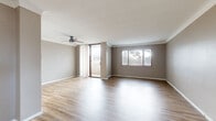 This 2-bedroom, 2-bathroom single-floor residence offers a thoughtfully organized layout that maximizes comfort and functionality. Hardwood-style flooring flows throughout the main living areas and bedrooms, complementing the neutral gray-toned walls for a clean, cohesive aesthetic.

The spacious living room is a standout feature, benefiting from abundant natural light through large windows and a sliding glass door that opens to an outdoor patio. A ceiling fan adds comfort to this open, airy space. Adjacent to the living room, the kitchen features light wood cabinetry with gold hardware, white tile flooring, a full suite of appliances including an electric range, built-in microwave, and dishwasher, all set against a tiled backsplash and ample counter space.

The primary bedroom is generously sized, featuring wide windows with vertical blinds and direct access to the patio through a sliding glass door, enhancing its sense of openness. The second bedroom is also well-proportioned with large windows offering outdoor views and the same warm hardwood-style flooring.

Two bathrooms serve the residence. One includes a glass-enclosed shower/tub combination with tile surround and a vanity with light wood cabinetry, while the second is a functional half-style bath with a single-basin vanity. A dedicated closet, entrance, and hallway round out this efficiently designed home.