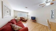 This single-floor home offers a well-organized layout that balances comfort and functionality throughout its rooms. The living room is an inviting, open space finished with light hardwood flooring and neutral walls that create a bright, airy atmosphere. A ceiling fan overhead adds to the room's comfort, while a large window dressed with blinds allows natural light to fill the space. The dining area features warm hardwood flooring and a pass-through window connecting to the kitchen, fostering a sense of openness and easy communication between spaces. A ceiling fan complements this area as well. The kitchen is laid out in a practical galley style, with white cabinetry, granite-look countertops, a white electric range, and tile flooring. A hallway leads conveniently from the kitchen toward additional rooms. The bedroom is a restful retreat with dark hardwood-style flooring, neutral gray walls, a ceiling fan, and a window with sheer curtains that allow soft, diffused light. The bathroom features classic white subway tile wainscoting, a clean white vanity, and a window with blinds, lending the room a timeless, tidy aesthetic. Throughout the home, consistent finishes and warm tones create a cohesive and welcoming environment.
