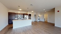 This well-appointed single-floor residence offers a thoughtfully designed open-concept layout that seamlessly connects the kitchen and living areas. The kitchen is a standout feature, showcasing rich dark-wood cabinetry with brushed nickel hardware, a mosaic tile backsplash, stainless steel appliances including a refrigerator, range, and microwave, and a generous white-countertop island with an undermount sink — ideal for both meal preparation and casual dining. Warm-toned wood-look flooring extends throughout the main living areas, lending a cohesive and contemporary feel.

The expansive living area is bathed in natural light, courtesy of large sliding glass doors that open to an outdoor balcony with views of the surrounding neighborhood. A ceiling fan adds comfort to this airy space. Conveniently tucked near the main living area is an in-unit stacked washer and dryer, maximizing space efficiency.

The bedroom is generously sized, featuring plush carpet, multiple large windows that invite abundant natural light, and a walk-in closet with built-in shelving. The bathroom is clean and modern, with dark cabinetry, a white countertop vanity, a large mirror, and a glass-enclosed shower with tile flooring. Overall, the space exudes a bright, neutral, and move-in-ready ambiance.