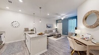 Located at 3061 Godwin Boulevard in Suffolk, Virginia, this single-floor residence offers a thoughtfully designed layout with modern finishes and a bright, welcoming ambiance throughout. The open-concept living and kitchen area serves as the heart of the home, where wood-look luxury vinyl plank flooring runs seamlessly underfoot. The kitchen is equipped with stainless steel appliances, white shaker-style cabinetry, granite countertops, and a central island with pendant lighting above — ideal for both meal preparation and casual dining with bar-stool seating along the extended counter. The living room features a bold teal accent wall that adds a pop of color against the neutral palette, complemented by a ceiling fan, natural light streaming through window blinds, and ample space for comfortable furnishings. The bedroom is finished with plush carpeting, neutral tones, and a window that invites natural light, creating a calm and restful retreat. The bathroom features wood-look flooring, a tub-shower combination, and clean, minimalist finishes. Throughout the space, five-panel interior doors, recessed lighting, and consistent color choices contribute to a cohesive, contemporary aesthetic that is both functional and visually appealing.