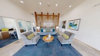 This well-appointed clubhouse offers a thoughtfully designed single-floor layout encompassing multiple functional areas for community use. The main lounge serves as the centerpiece of the space, showcasing dramatic soaring ceilings, recessed lighting, and a striking floor-to-ceiling diagonal wood lattice partition that adds architectural character and visual depth. Comfortable striped armchairs and a plush sofa arranged around a round coffee table on a blue area rug create an inviting gathering area, complemented by framed artwork on the walls.

The reception and entry area features an impressive wall of large windows that flood the polished concrete floors with abundant natural light, creating an open and airy atmosphere. A welcoming front desk area with glass doors provides a professional point of contact for residents.

The kitchenette is equipped with granite countertops, dark cabinetry, glossy subway tile backsplash, a stainless steel refrigerator, and a coffee station — ideal for casual refreshments and community gatherings.

The fitness center is fully outfitted with treadmills, elliptical machines, a comprehensive free-weight rack, medicine balls, and a wall-mounted television. Ceiling fans, carpeted flooring, and windows with natural light make the workout space both functional and comfortable. Together, these areas create a versatile and welcoming clubhouse environment.