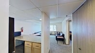 Located at 646 East College Avenue in State College, PA, this 490-square-foot apartment offers a practical and efficient single-floor layout well-suited for student occupancy. The living area features carpeted flooring, neutral walls, a wall-mounted PTAC heating and cooling unit, and a large window with vertical blinds that allows natural light to fill the space. The kitchen is equipped with wooden cabinetry, a black refrigerator, a gas range, a sink, and a microwave. A wraparound granite-style countertop doubles as a breakfast bar with two wooden stools, creating a functional and social dining space. The apartment includes two bedrooms, each carpeted and furnished with twin beds featuring built-in drawer storage underneath, maximizing the use of limited square footage. Both rooms are bright, with windows providing natural light, and feature textured ceilings. The full bathroom contains a combination tub and shower, a toilet, and a wall mirror, finished with tile-style flooring. Throughout the unit, the design is straightforward and utilitarian, prioritizing functionality and space efficiency — characteristic of student housing near Penn State University.