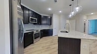 Located at 870 S SH 161 Frontage Rd in Grand Prairie, TX, this well-appointed 2-bedroom, 2-bathroom residence offers a thoughtfully designed single-floor layout with modern finishes throughout. The open-concept kitchen and living area serves as the heart of the home, showcasing rich dark cabinetry, sleek granite countertops, a large center island with a undermount sink, and stainless steel appliances including a range, microwave, and refrigerator. Globe pendant lights add a contemporary touch above the island, while light wood-style flooring flows seamlessly throughout the common areas. The living room features French doors that invite natural light and provide outdoor access, complemented by a ceiling fan overhead. Both bedrooms are carpeted for comfort, with the spacious primary bedroom offering generous proportions and access to a well-sized walk-in closet outfitted with multi-level shelving. The bathrooms are finished with granite-topped dark vanities and marble-style tiled tub-shower surrounds. A second closet provides additional storage. The clean, neutral color palette and consistent use of quality materials throughout give the space a cohesive, modern aesthetic.