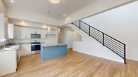 Located at 4235 Cameo Lane in Bellingham, Washington, this contemporary three-story townhome is designed with clean lines, a neutral palette, and thoughtful finishes throughout. The main living level showcases an open-concept layout with light hardwood flooring that flows seamlessly from the kitchen through to the living area. The kitchen is a standout feature, equipped with white shaker cabinetry, stainless steel appliances including a range, microwave, and dishwasher, light quartz countertops, and a striking blue center island with pendant lighting above. The adjacent living area offers a sleek, built-in fireplace and a modern staircase with a bold black metal railing that serves as an architectural focal point. Upper-level bedrooms are finished with plush carpet, generous closet space — including a walk-in closet — and individual wall-mounted climate control units for personalized comfort. A well-appointed bathroom features a soaking tub, updated vanity with white cabinetry, and a window framing lush, natural greenery. The outdoor balcony extends the living space with views of a landscaped yard and a mature, wooded backdrop. This townhome blends modern design with a tranquil Pacific Northwest setting.