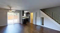 This two-story home offers a thoughtfully designed layout that balances comfort and functionality across two levels. The main floor showcases an open-concept living and kitchen area unified by rich, dark hardwood flooring that extends throughout the space. Large sliding glass doors flood the living area with natural light while providing direct access to an outdoor patio, offering a seamless indoor-outdoor connection. A ceiling fan overhead adds to the comfort of the living space.

The kitchen is well-appointed with dark espresso cabinetry, a mosaic tile backsplash, stainless steel appliances, and a peninsula that serves as both a prep surface and a casual gathering spot. A window above the sink brings in additional natural light. A door off the kitchen leads to a utility or additional room, offering extra convenience.

A staircase with a classic white balustrade leads to the second floor, where additional living quarters are situated. A built-in nook beneath the stairs adds a charming architectural detail. The overall ambiance of the home is clean and modern, with neutral gray walls and white trim complementing the dark wood tones throughout, creating a cohesive and inviting atmosphere.