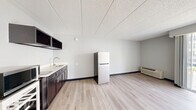 Located at 1722 N Walnut St, Unit 207 in Bloomington, Indiana, this compact studio unit offers an efficient, single-floor layout designed to maximize functionality. The open living area features light-toned hardwood flooring and neutral gray walls, creating a clean, bright atmosphere throughout. A drop tile ceiling runs the length of the space, and a wall-mounted HVAC unit provides climate control.

The kitchenette area is well-appointed with dark cabinetry, open upper shelving, a stainless steel sink, and a full-size refrigerator, offering practical amenities within a streamlined footprint. The living space flows seamlessly from the kitchen area, providing flexibility in how the room is arranged and used.

Natural light enters generously through a large sliding glass door that opens onto a private balcony, offering views of the surrounding neighborhood and greenery — a standout feature that enhances the overall sense of openness in the unit.

The bathroom is accessed through a wood-panel door and features light hardwood-style flooring, white tile walls, and a full tub and shower combination, keeping the design clean and functional.

Overall, this unit presents a well-maintained, efficient living space with modern finishes, making it a practical option in the Bloomington, IN area.