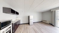 Located at 1722 N Walnut St, Unit 207 in Bloomington, Indiana, this compact studio unit offers an efficient, single-floor layout designed to maximize functionality. The open living area features light-toned hardwood flooring and neutral gray walls, creating a clean, bright atmosphere throughout. A drop tile ceiling runs the length of the space, and a wall-mounted HVAC unit provides climate control.

The kitchenette area is well-appointed with dark cabinetry, open upper shelving, a stainless steel sink, and a full-size refrigerator, offering practical amenities within a streamlined footprint. The living space flows seamlessly from the kitchen area, providing flexibility in how the room is arranged and used.

Natural light enters generously through a large sliding glass door that opens onto a private balcony, offering views of the surrounding neighborhood and greenery — a standout feature that enhances the overall sense of openness in the unit.

The bathroom is accessed through a wood-panel door and features light hardwood-style flooring, white tile walls, and a full tub and shower combination, keeping the design clean and functional.

Overall, this unit presents a well-maintained, efficient living space with modern finishes, making it a practical option in the Bloomington, IN area.