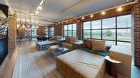 Located at 601 Meeting Street in Charleston, SC, this thoughtfully designed amenity space blends industrial character with modern comfort. Exposed brick walls, high ceilings, and large steel-framed windows define the architectural identity throughout, flooding the interior with natural light and offering expansive views of the surrounding Charleston landscape.

The main lounge area features soaring double-height ceilings, floor-to-ceiling windows, and a dramatic reclaimed wood accent wall housing a mounted flat-screen television. Generous sectional seating, warm leather accent chairs, and layered rugs create an inviting atmosphere ideal for gathering or relaxing.

A secondary lounge area offers a more casual setting with plaid upholstered ottomans, built-in bench seating, and track lighting, all framed by large windows that bring in ample daylight and scenic outdoor views.

The fully equipped kitchen serves as the heart of the space, featuring a spacious quartz-topped island with bar seating, stainless steel appliances, open wood shelving, a patterned tile floor, and bold pendant lighting suspended from an exposed ceiling. An additional lounge adjacent to the kitchen includes leather sofas centered around a wall-mounted television, anchored by a dark accent wall and complementary brick detailing. A dining area with a round wood table completes the space.