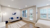 This thoughtfully designed studio unit offers a well-organized, open-concept floor plan that maximizes every square foot across a single level. Light wood-style flooring flows continuously throughout, complementing the neutral gray and white color palette that lends the space a clean, contemporary feel. Recessed lighting illuminates each area, while multiple windows fitted with horizontal blinds invite generous natural light and outdoor views.

The kitchen is a standout feature, outfitted with warm wood-toned cabinetry, black hardware accents, white subway tile backsplash, and a full suite of stainless steel appliances including a range, microwave, dishwasher, and refrigerator. A marble-topped breakfast bar provides additional prep and dining space. The kitchen flows seamlessly into the living area, which accommodates a sofa, wall-mounted television, and decorative accents, creating a comfortable lounge setting.

The sleeping area is positioned near a large window that fills the space with natural light, offering a bright and restful retreat. A wall-mounted shelf above the bed adds both function and style. The private bathroom features a wood-toned vanity with a white countertop, a large framed mirror, and a glass-enclosed walk-in shower with tile surround, completing this polished and practical unit.
