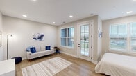 This thoughtfully designed studio unit offers a well-organized, open-concept floor plan that maximizes every square foot across a single level. Light wood-style flooring flows continuously throughout, complementing the neutral gray and white color palette that lends the space a clean, contemporary feel. Recessed lighting illuminates each area, while multiple windows fitted with horizontal blinds invite generous natural light and outdoor views.

The kitchen is a standout feature, outfitted with warm wood-toned cabinetry, black hardware accents, white subway tile backsplash, and a full suite of stainless steel appliances including a range, microwave, dishwasher, and refrigerator. A marble-topped breakfast bar provides additional prep and dining space. The kitchen flows seamlessly into the living area, which accommodates a sofa, wall-mounted television, and decorative accents, creating a comfortable lounge setting.

The sleeping area is positioned near a large window that fills the space with natural light, offering a bright and restful retreat. A wall-mounted shelf above the bed adds both function and style. The private bathroom features a wood-toned vanity with a white countertop, a large framed mirror, and a glass-enclosed walk-in shower with tile surround, completing this polished and practical unit.