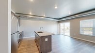 Located in Aberdeen, SD, this 3-bedroom, 1-bathroom unit offers a well-designed, single-floor layout that makes efficient use of its space. The open-concept kitchen and living area serves as the heart of the unit, anchored by a central island with a granite countertop and an integrated sink. Dark-toned cabinetry with brushed gold hardware lines the kitchen walls, complemented by stainless steel appliances including a refrigerator, range, microwave, and dishwasher. Light wood-tone flooring runs throughout the main living area, contributing to a clean, modern aesthetic. Exposed metallic ductwork adds an industrial design element along the ceiling perimeter. The living room is bathed in natural light through large sliding glass doors that open to a private balcony with views of the surrounding neighborhood, alongside an additional window. The three bedrooms feature neutral carpet flooring and soft, warm-toned walls, offering a comfortable retreat. The bathroom includes a walk-in shower with grab bars, light tile flooring, and a tile-paneled ceiling, providing a functional and accessible design. Overall, the unit presents a contemporary, move-in-ready space with consistent finishes throughout.
