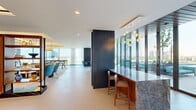 Located at 9 Harrington St in downtown Raleigh, NC, this elegantly designed amenity floor spans an expansive single level, offering a refined blend of social, work, and outdoor living spaces. The open-plan interior is anchored by a generous lounge area with coffered ceilings, ambient lighting, and a built-in wood and marble entertainment wall. Plush seating arrangements, contemporary pendant fixtures, and floor-to-ceiling glass walls flood the space with natural light while framing panoramic views of the Raleigh skyline. A sleek kitchen bar features dramatic stone countertops, warm wood cabinetry, and pendant globe lighting, seamlessly connecting to the lounge and dining areas. A flexible co-working zone includes casual seating, a printer station, and bar-height counters along the window line. Private rooms cater to focused work, including a boutique conference room with a wall-mounted display and pendant lighting, and an acoustically treated lounge room with padded walls ideal for quiet meetings. The outdoor rooftop terrace is a standout feature, boasting a resort-style pool, sculptural lounge chairs, pergola-shaded seating, and breathtaking views of the downtown Raleigh cityscape — an exceptional space for both work and leisure.