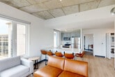 Located at 2–4 N Park St in Madison, WI, this spacious 7-bedroom, 4-bathroom unit offers a well-designed layout across a single floor. The open-concept living and kitchen area serves as the heart of the unit, featuring an exposed concrete ceiling that lends an industrial aesthetic, light wood-style flooring, and large windows that flood the space with natural light and offer elevated views of the Madison cityscape. The kitchen is outfitted with gray cabinetry, stainless steel appliances including a refrigerator, microwave, and electric range, and a generous white quartz island with an undermount sink — ideal for both cooking and communal dining. The living room includes a concrete structural column as an architectural accent, reinforcing the modern industrial character of the space. Each of the seven bedrooms is a compact, functional space with carpeted flooring, large windows with city views, and furnishings that include a bed, desk, dresser, and chair. The four bathrooms are clean and contemporary, featuring frameless glass walk-in showers, white undermount sinks, and large mirrors. Hallways are accented with board-formed concrete wall panels, tying together the unit's cohesive industrial-modern design throughout.