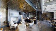 This single-floor Dallas space masterfully combines industrial and rustic design elements to create a sophisticated, layered environment. The ceiling is a standout feature, finished with warm wood planking that contrasts beautifully against exposed metal ductwork and structural elements, lending the space an authentic loft-like character.

The open layout is thoughtfully divided into distinct functional zones. A comfortable lounge area anchors one side of the space, furnished with neutral-toned armchairs and a low coffee table arranged around a modern fireplace with a clean, minimalist surround. This area invites relaxed conversation and informal gatherings.

Adjacent to the lounge, a dedicated workspace is defined by steel-framed glass partitions with a dark metal finish, creating a semi-enclosed office area without sacrificing the open feel of the overall space. A wooden work surface runs along the interior, accompanied by task lighting and office equipment.

Throughout, wide-plank hardwood floors in a weathered finish unify the zones, while pendant and recessed lighting ensure warm, layered illumination. The overall ambiance is refined yet grounded, balancing professional functionality with inviting warmth.