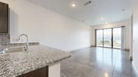 This single-floor unit showcases a clean, contemporary design defined by polished concrete floors that run consistently throughout the entire space, lending a cohesive and industrial-modern aesthetic. The open-concept living and dining area is bright and spacious, with crisp white walls, recessed lighting, and a large sliding glass door that opens to sweeping panoramic views of the surrounding landscape, flooding the interior with natural light.

The kitchen is efficiently designed with dark espresso cabinetry, a tile backsplash, granite countertops, and a full suite of stainless steel appliances including a refrigerator, range, and built-in microwave. A peninsula counter extends into the living area, creating a natural transition between cooking and living spaces.

The bedrooms are well-proportioned, each featuring large windows with outdoor views and continued polished concrete flooring. The bathroom is finished with a dark vanity topped with granite, a full tub-shower combination with white tile surround, and a mirror above the sink. Additional storage is provided by a generously sized walk-in closet equipped with multiple shelving and hanging rod systems.