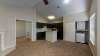 This single-floor space is designed with an open-concept layout that connects the living area and kitchen, creating a cohesive and functional flow throughout. The kitchen is a standout feature, outfitted with dark espresso cabinetry that extends to the upper walls, providing generous storage. Speckled light granite-style countertops contrast the dark cabinetry, and a peninsula island offers additional prep space and casual seating potential. Black appliances — including a refrigerator, range, microwave, and dishwasher — complete the kitchen's cohesive look. Wood-style flooring anchors the kitchen area, while neutral carpet extends throughout the living space and bedroom. A ceiling fan is positioned in the living area, adding both function and a finishing touch to the space. A dedicated laundry alcove with stacked washer/dryer connections is conveniently located just off the main living area. The bathroom features dark cabinetry with a speckled countertop vanity, a tiled tub-shower combination, and wood-style flooring. The carpeted bedroom is a comfortable retreat with a ceiling fan and a window that brings in natural light and outdoor views.
