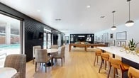 This thoughtfully designed community lounge offers a generous, open-plan layout across a single floor, seamlessly blending modern aesthetics with multi-functional living. Light hardwood flooring flows throughout the entire space, creating a warm and cohesive foundation that ties each zone together.

At the heart of the room, a bold black built-in entertainment wall serves as a dramatic focal point, housing a large flat-screen TV, decorative shelving, and curated décor. In front of it, a richly upholstered amber sofa accented with teal throw pillows anchors a relaxed lounge area, complemented by plush accent chairs and a patterned area rug. Adjacent to this, a full-length shuffleboard table provides a central gaming feature.

A dedicated dining area near the entrance features round marble-topped tables and woven chairs, positioned alongside striking textured black accent walls adorned with a geometric diamond pattern. Floor-to-ceiling sliding glass doors open directly to an outdoor pool area, flooding the space with natural light and offering seamless indoor-outdoor connectivity.

A well-appointed kitchenette along one wall includes dark cabinetry, a white countertop island with bar seating, a textured tile backsplash, stainless steel appliances, and globe pendant lighting. A gallery wall of framed artwork lines the perimeter, adding a curated, artistic dimension to the overall ambiance.