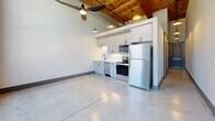 Located at 250 S Depot St in Pendleton, South Carolina, this thoughtfully designed unit blends historic industrial character with modern finishes. The main living area immediately impresses with soaring ceilings accented by warm wood planking and exposed ductwork, polished concrete floors that reflect natural light, and dramatic exposed brick walls. Large arched and grid-pane windows flood the space with abundant natural light while framing views of the surrounding outdoor environment, creating an open and airy atmosphere enhanced by a ceiling fan overhead.

The kitchen is efficiently laid out along one wall, featuring white shaker-style cabinetry, stainless steel appliances including a refrigerator, range, microwave, and dishwasher, and a clean subway tile backsplash. Pendant lighting and a wood-beamed ceiling overhead give the kitchen area a warm, inviting character that contrasts beautifully with the industrial elements throughout.

A hallway leads to the bathroom, which is finished with polished concrete floors, a vanity with storage, and modern matte black hardware and fixtures. A barn-style sliding door adds a stylish, space-conscious touch. Throughout the unit, the interplay of raw brick, natural wood, and contemporary fixtures delivers a cohesive urban-industrial aesthetic.