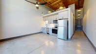 Located at 250 S Depot St in Pendleton, South Carolina, this thoughtfully designed unit blends historic industrial character with modern finishes. The main living area immediately impresses with soaring ceilings accented by warm wood planking and exposed ductwork, polished concrete floors that reflect natural light, and dramatic exposed brick walls. Large arched and grid-pane windows flood the space with abundant natural light while framing views of the surrounding outdoor environment, creating an open and airy atmosphere enhanced by a ceiling fan overhead.

The kitchen is efficiently laid out along one wall, featuring white shaker-style cabinetry, stainless steel appliances including a refrigerator, range, microwave, and dishwasher, and a clean subway tile backsplash. Pendant lighting and a wood-beamed ceiling overhead give the kitchen area a warm, inviting character that contrasts beautifully with the industrial elements throughout.

A hallway leads to the bathroom, which is finished with polished concrete floors, a vanity with storage, and modern matte black hardware and fixtures. A barn-style sliding door adds a stylish, space-conscious touch. Throughout the unit, the interplay of raw brick, natural wood, and contemporary fixtures delivers a cohesive urban-industrial aesthetic.