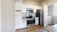 This two-floor residence offers a practical and well-organized layout across its two levels. The ground floor houses a private garage equipped with an automatic opener, providing secure parking and additional storage space with a concrete floor. The main living level upstairs encompasses the majority of the home's footprint, connecting all primary living areas via a carpeted staircase and hallway.

The kitchen is a standout feature, designed in a galley style with white cabinetry extending to the ceiling for ample storage. Granite countertops and a full suite of stainless steel appliances — including a refrigerator, electric range, built-in microwave, and dishwasher — complete the space. Wood-look flooring runs throughout, and a charming arched window above the entry door brings in natural light.

The bedroom is generously sized, finished with plush carpeting, neutral toned walls, and a ceiling fan with light fixture. A window with blinds offers outdoor views and natural light. The adjacent bathroom features a granite-topped vanity, wood-look flooring, and a tiled shower-tub combination. A dedicated closet and a separate laundry area — outfitted with a top-load washer and overhead wire shelving — round out the upper floor's functional amenities.